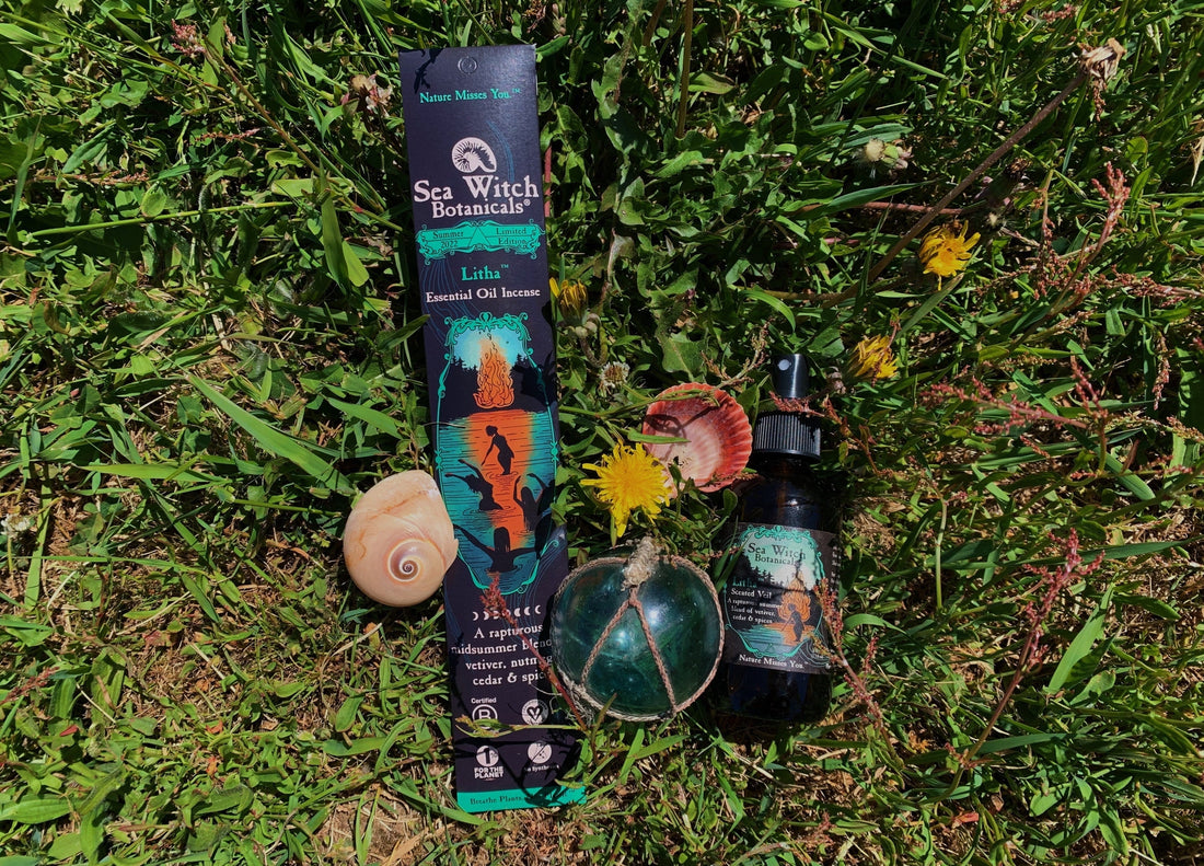 Litha incense & spray laying in grass with dandelions, seashells, and blue glass ball wrapped in rope