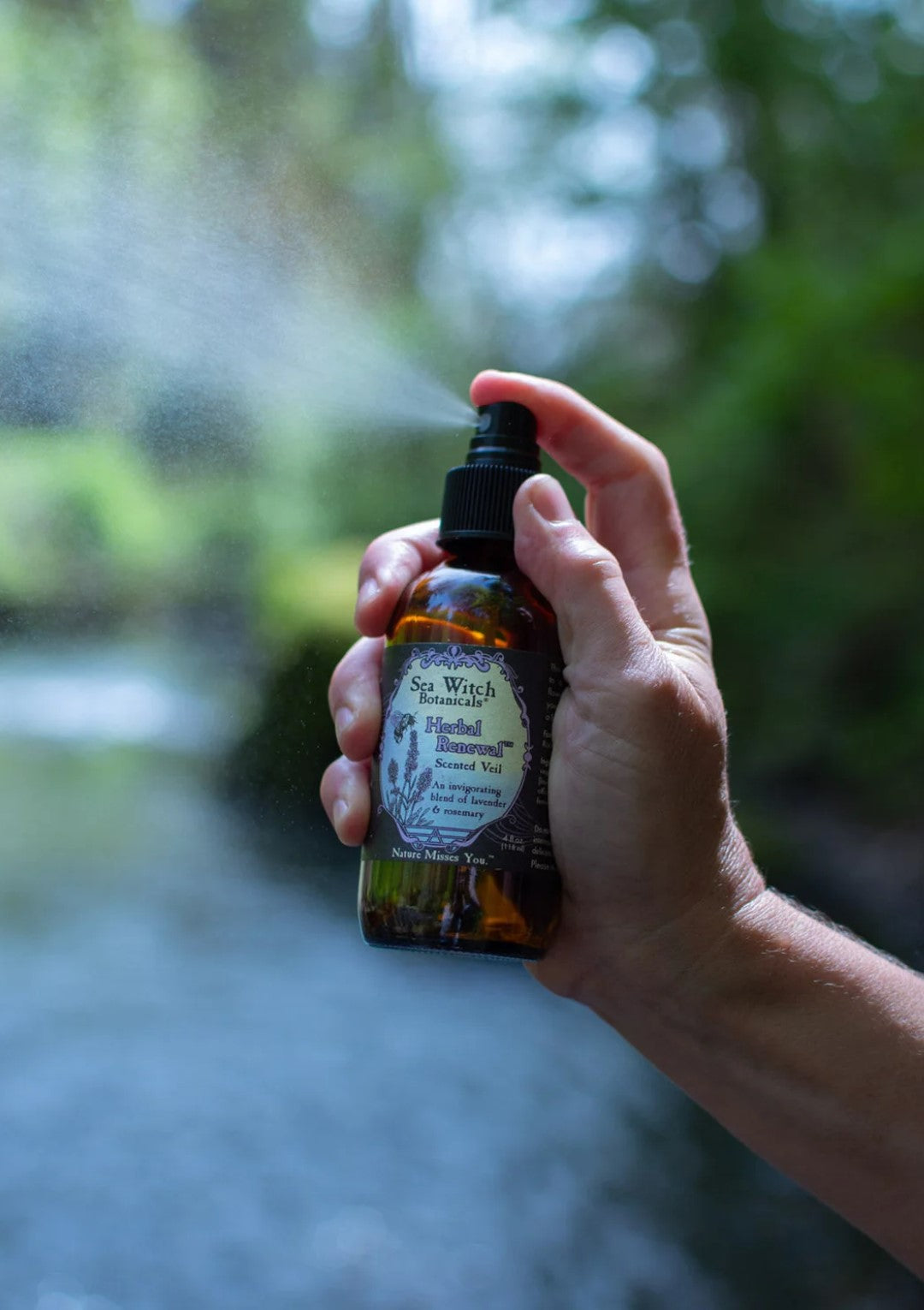 Closeup of someone spraying an Herbal Renewal scented veil, lake in the background.