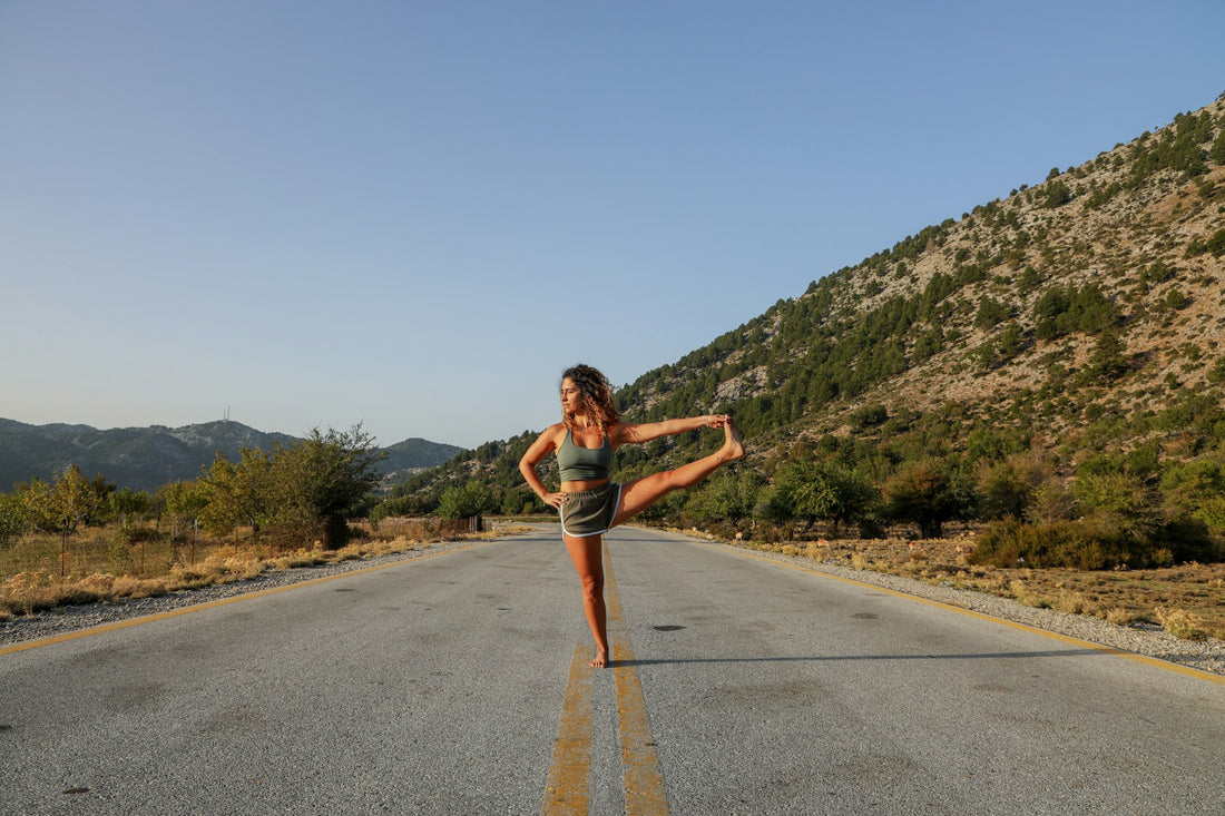 Woman in tank top and denim shorts stretching and standing on gray asphalt.