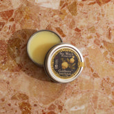 Small tin of balm with a decorative label on a textured surface