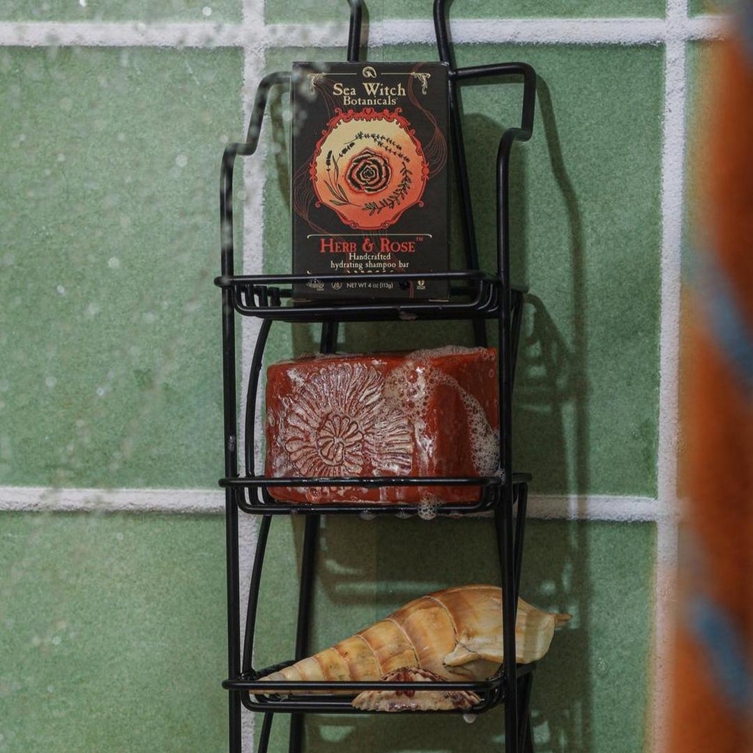 Three-tiered black metal wall shelf with decorative items against a green tiled wall.