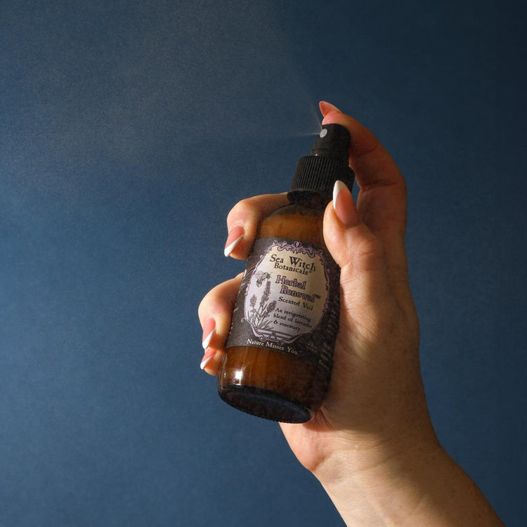 Hand holding a brown spray bottle with a label against a dark blue background