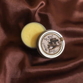 Small jar of balm with a decorative label on a brown fabric background