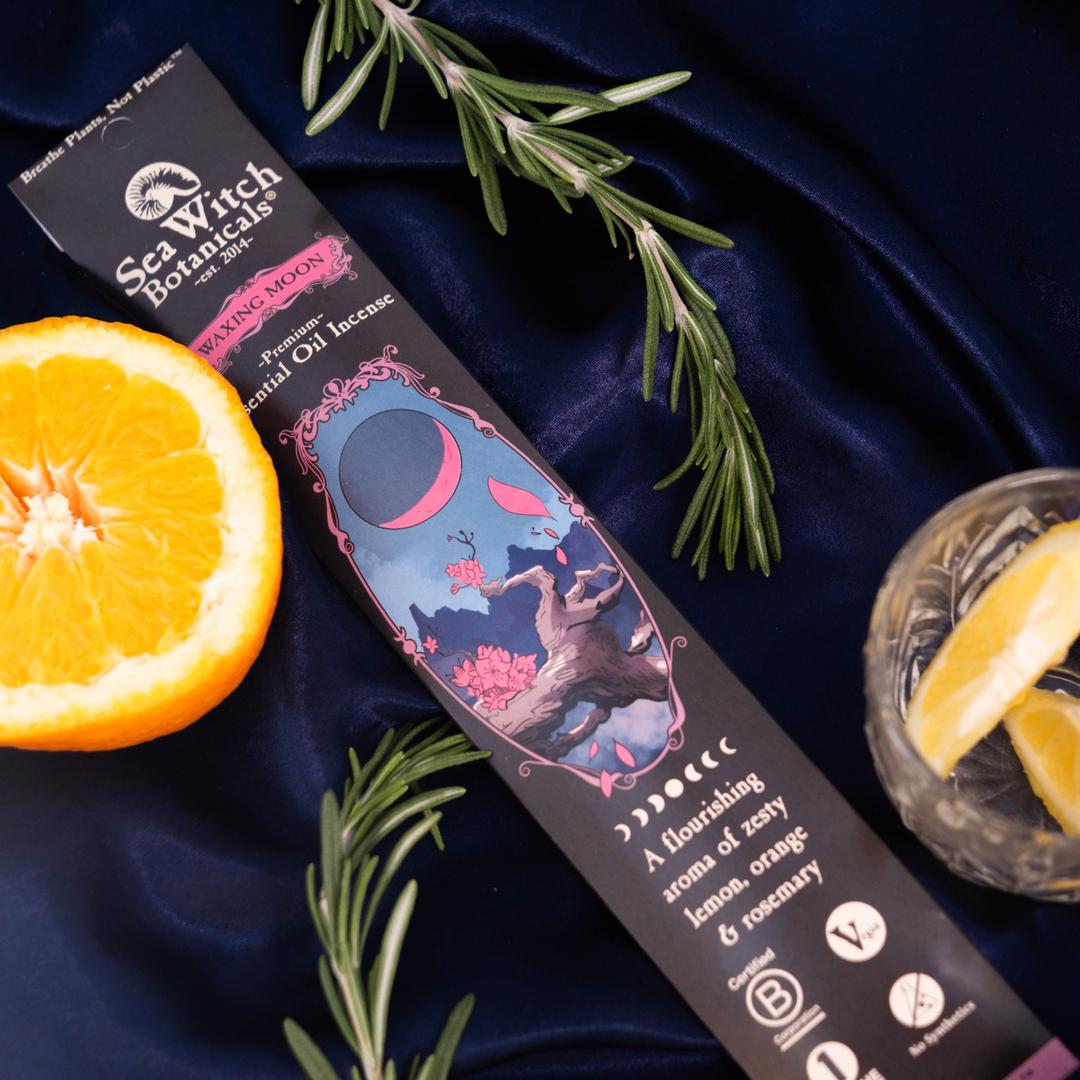 Sea Witch Remedies product packaging on a dark blue fabric background with an orange and rosemary.
