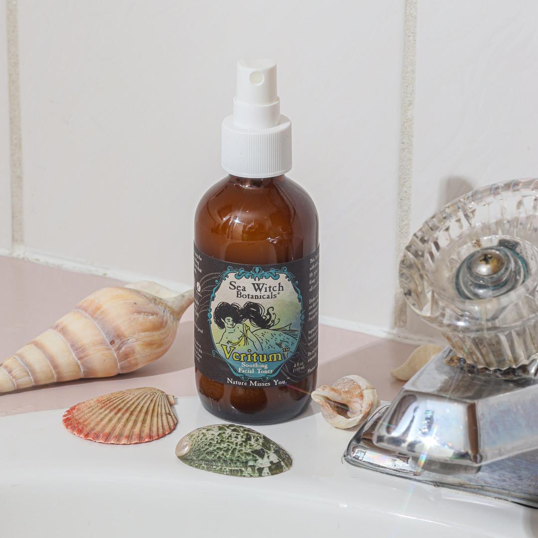 Bottle of Sea Witch Veritumspray on a bathroom counter with shells and a faucet.