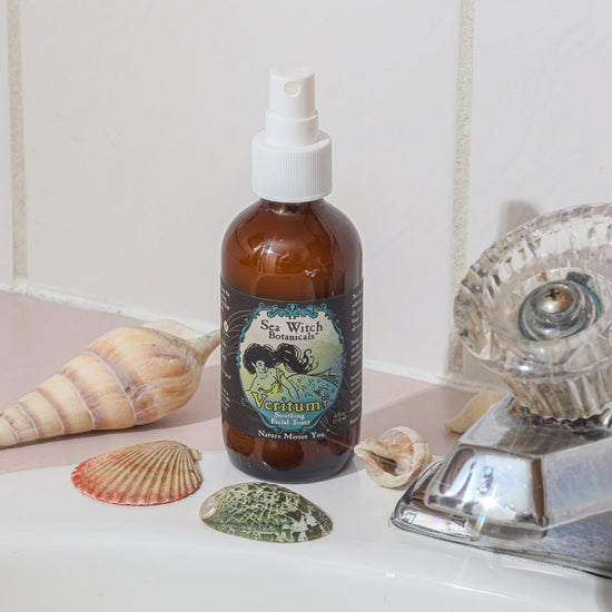 Bottle of Sea Witch Veritumspray on a bathroom counter with shells and a faucet.