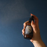 Hand holding a dark glass bottle with a dropper against a dark blue background